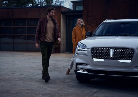 A man and a woman approaching a 2024 Lincoln Aviator® SUV, which illuminates certain lights when they are close | Hooks Lincoln in Fort Worth TX
